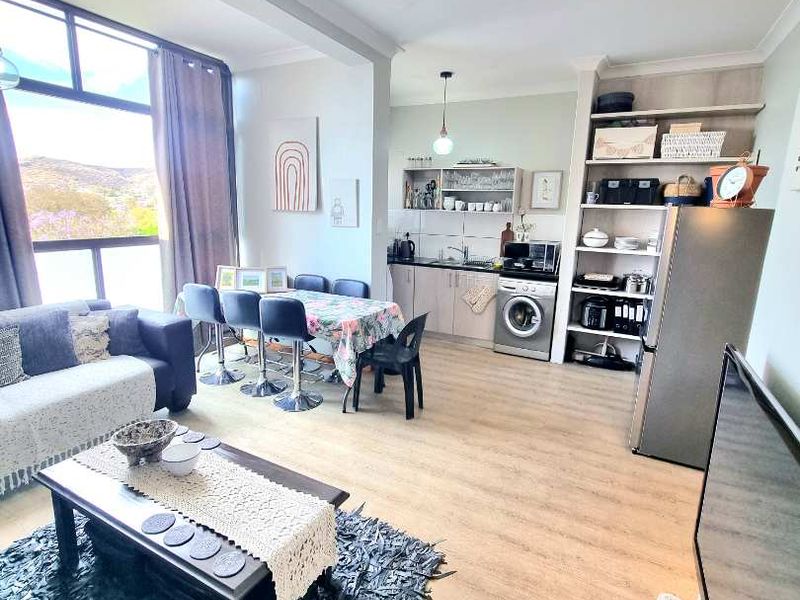 An open-plan living and kitchen area featuring light laminate flooring, built-in cabinetry, and large windows providing natural light and scenic views.