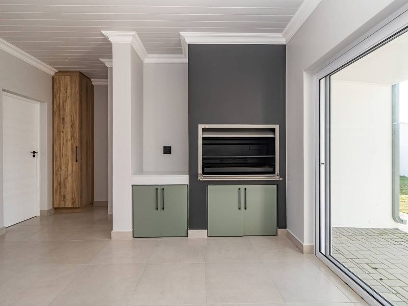 Modern living area featuring a built-in braai, sage green cabinetry, tiled floors, and large sliding doors opening to an outdoor space.