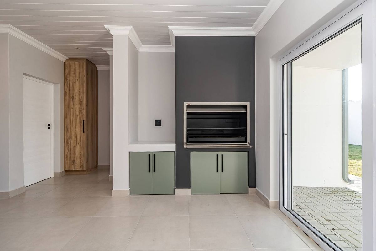Modern living area featuring a built-in braai, sage green cabinetry, tiled floors, and large sliding doors opening to an outdoor space.