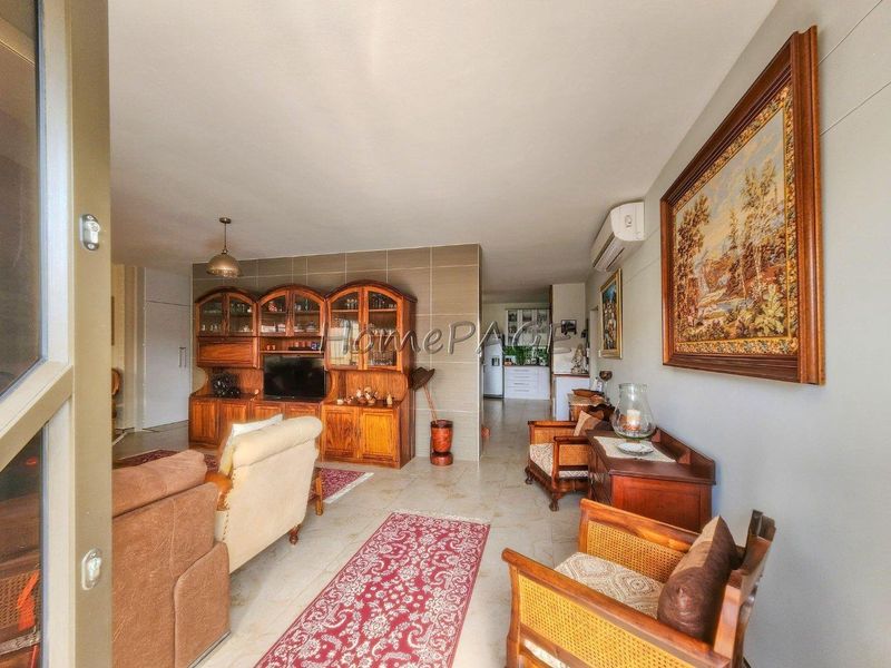 Open-plan living area featuring tiled flooring, a tiled feature wall, and a wall-mounted air conditioning unit, leading through to the kitchen area.
