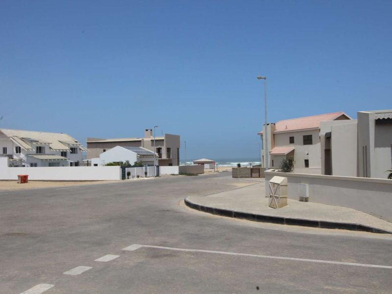 A street view of a coastal residential neighbourhood showing paved roads, boundary walls, and proximity to the ocean.