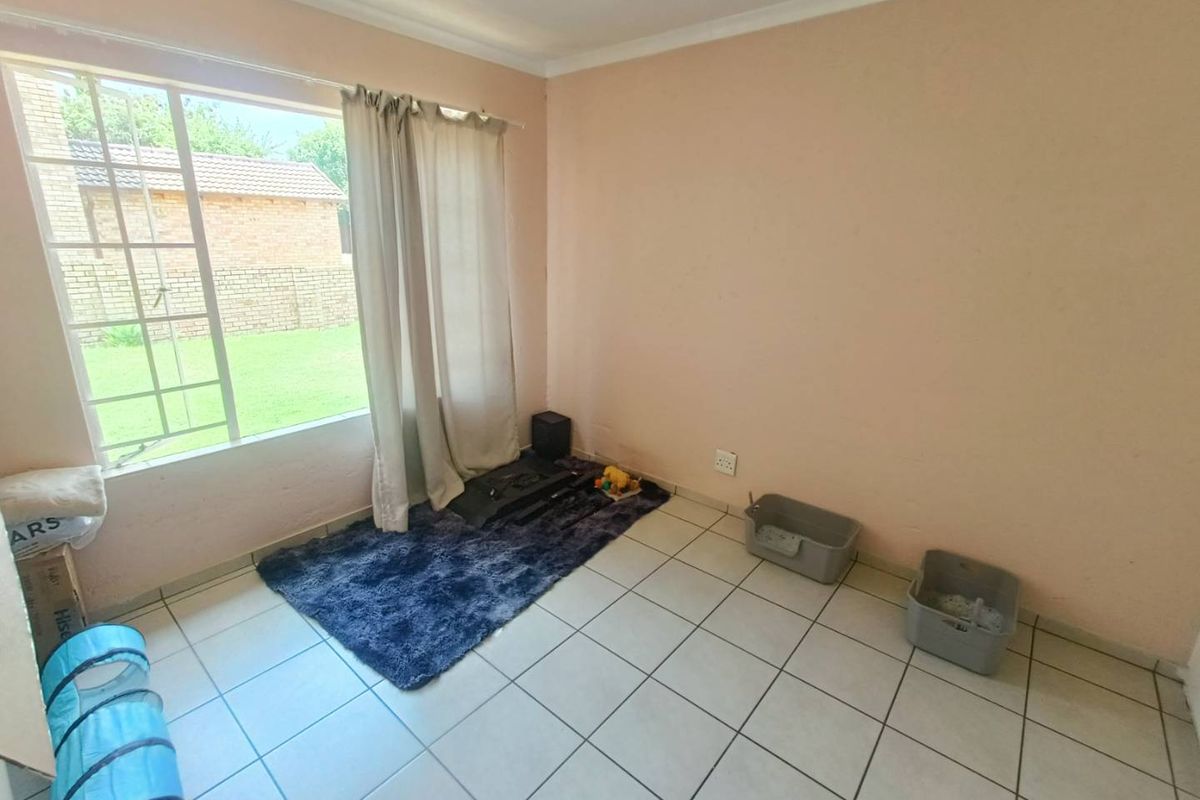 A simple bedroom featuring tiled flooring and a large window with security bars, offering a view of the rear garden area.