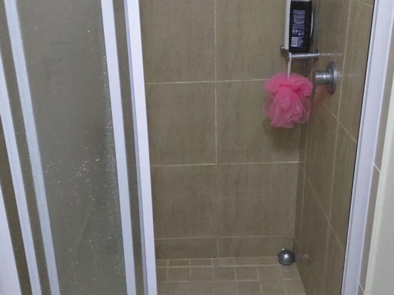 A functional bathroom shower enclosure featuring neutral wall and floor tiling with a glass door entry.