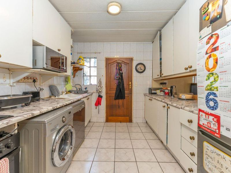 A functional kitchen featuring laminate countertops, tiled flooring, and ample built-in cabinetry, providing a practical workspace with direct access to an exterior door.