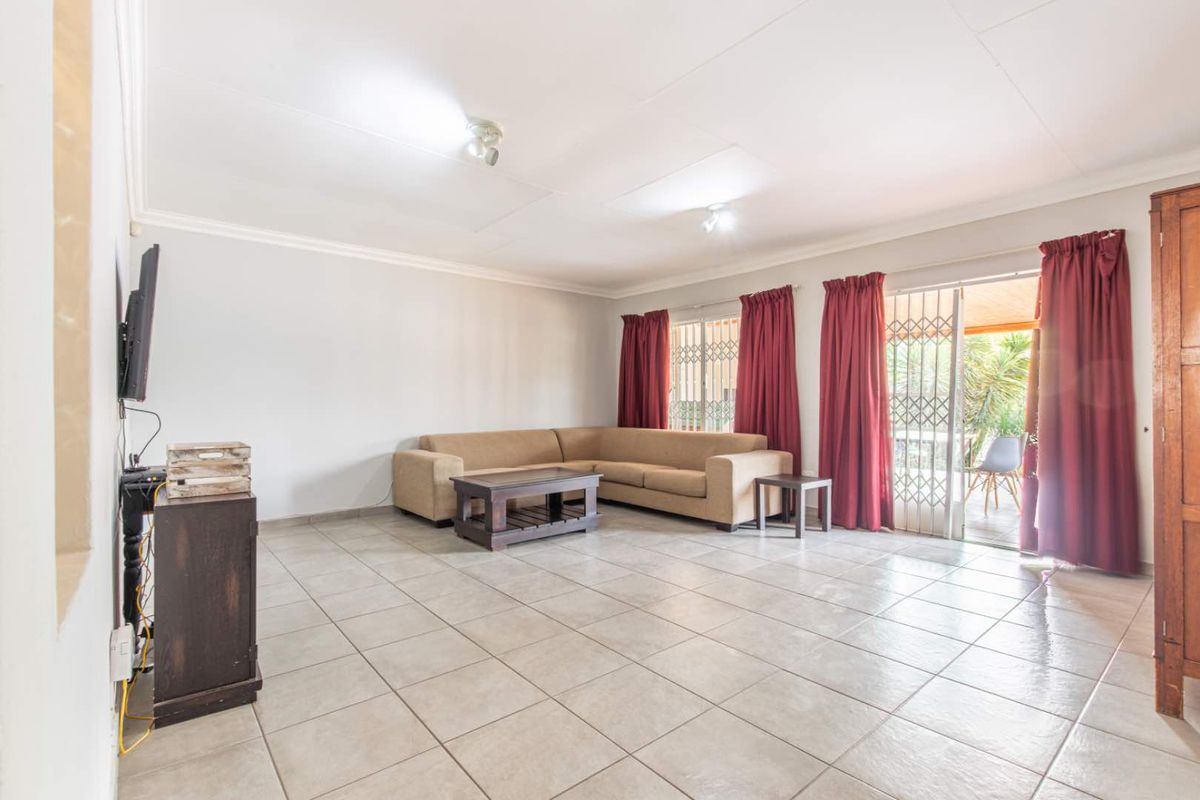 Spacious living room featuring neutral floor tiles, ceiling-mounted lighting, and sliding glass doors providing direct access to the outdoor patio area.