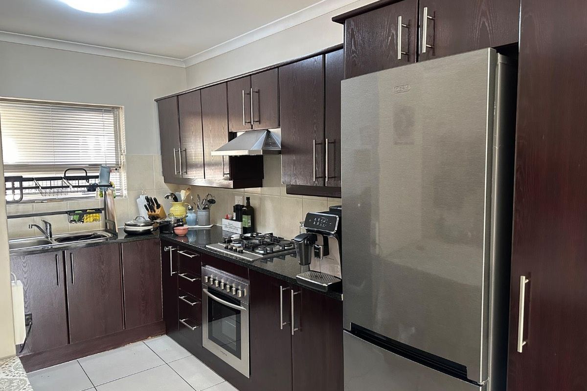 A functional kitchen featuring dark wood cabinetry, granite countertops, a gas hob, built-in oven, and tiled flooring.