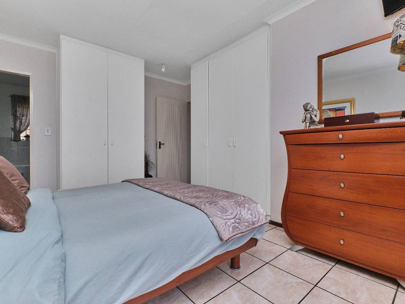 A functional bedroom featuring built-in cupboards, tiled flooring, and coved cornicing, offering a clean and practical living space.