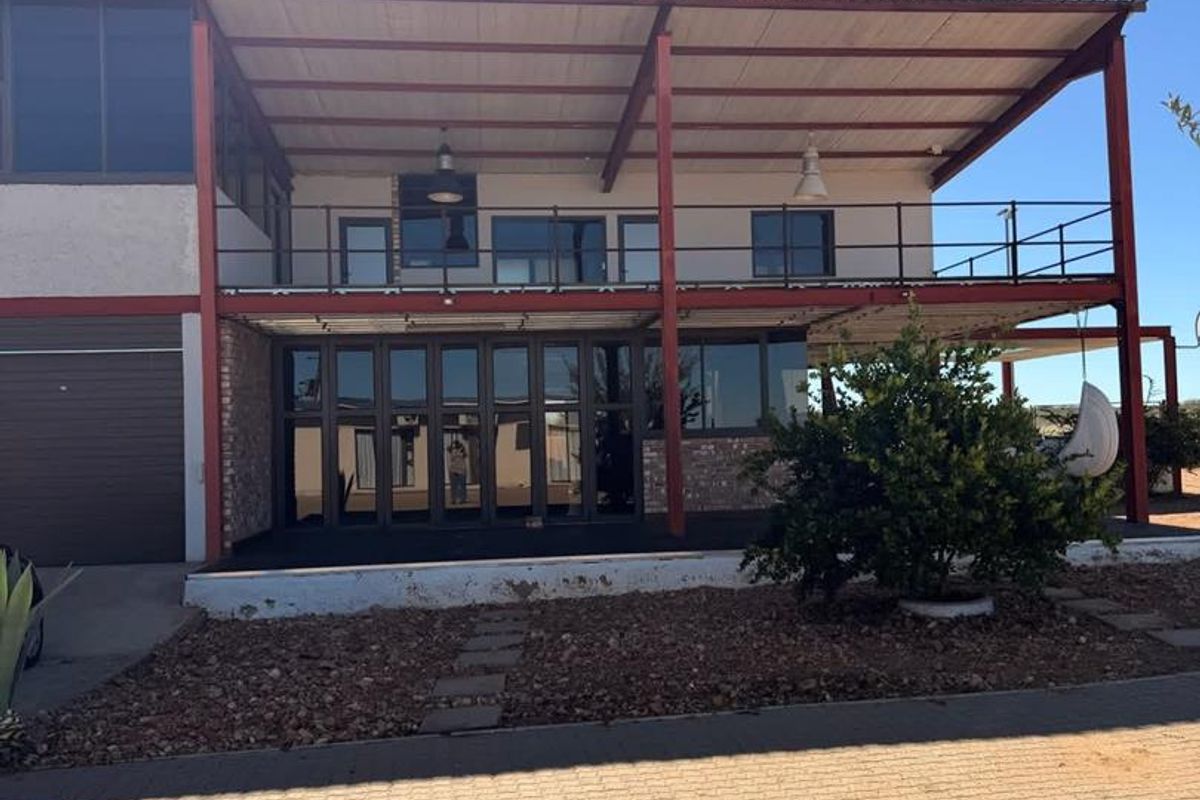 Exterior view of a farm property featuring a large covered patio area, steel structural framing, and expansive glass folding doors.