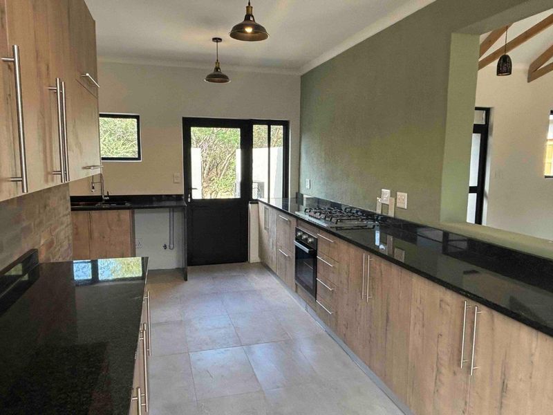 Modern kitchen featuring wood-finish cabinetry, sleek black granite countertops, a gas hob, built-in oven, and tiled flooring with direct outdoor access.