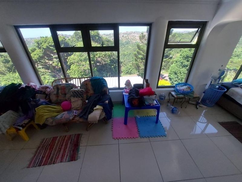 A bright living area featuring large windows with scenic views and neutral tiled flooring, offering a spacious layout with abundant natural light.