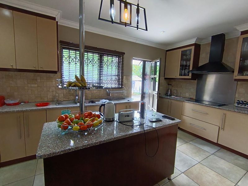 A functional kitchen featuring granite countertops, built-in cabinetry, a stainless steel extractor fan, and tiled flooring with direct access to the exterior.