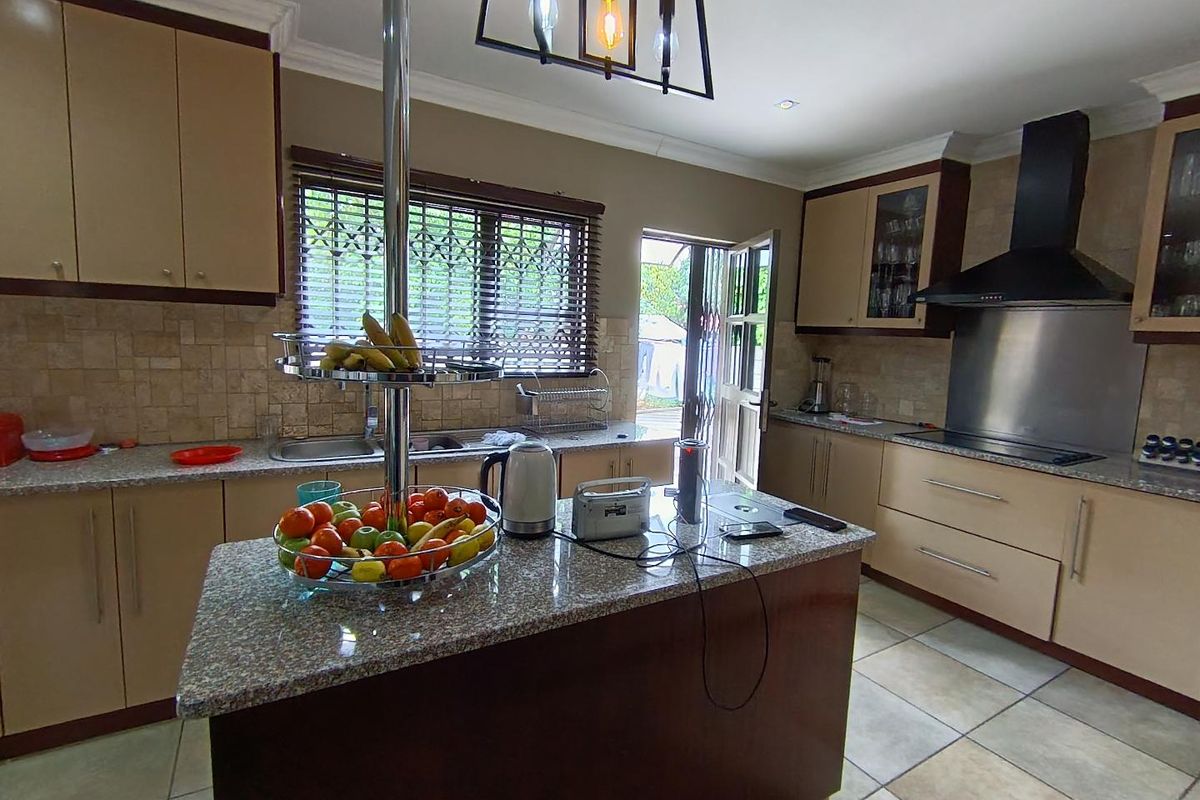 A functional kitchen featuring granite countertops, built-in cabinetry, a stainless steel extractor fan, and tiled flooring with direct access to the exterior.