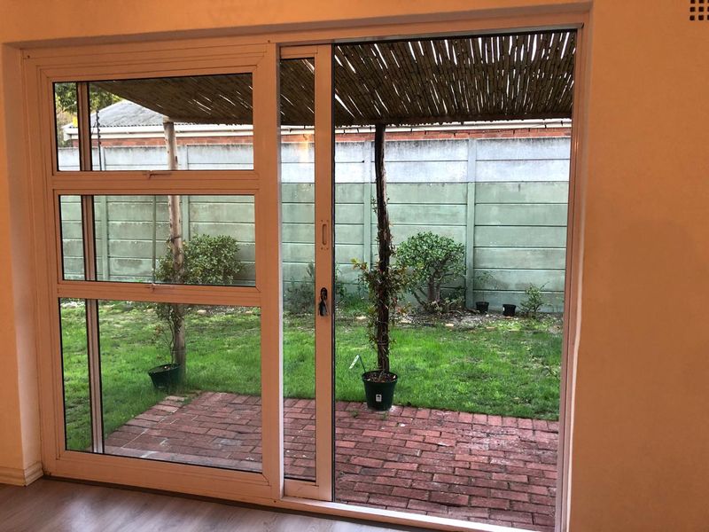 View from an interior space looking out onto a private brick patio, small garden area, and a covered bamboo pergola structure.