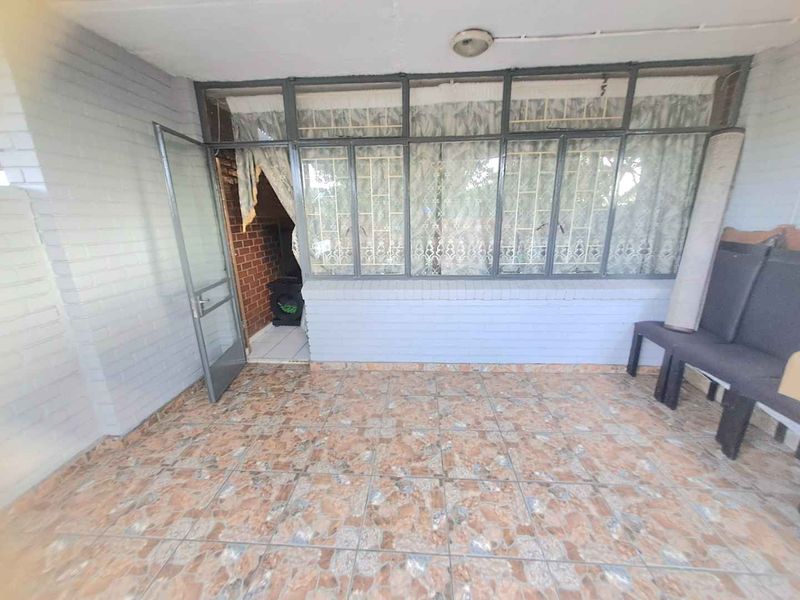 An enclosed patio area featuring tiled flooring, painted brick walls, and large metal-framed windows with security bars.