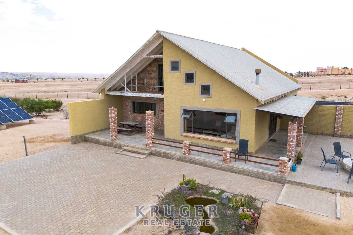 Aerial view of a modern small holding residence featuring a covered patio, brick-paved driveway, and solar panel installation in a rural landscape.