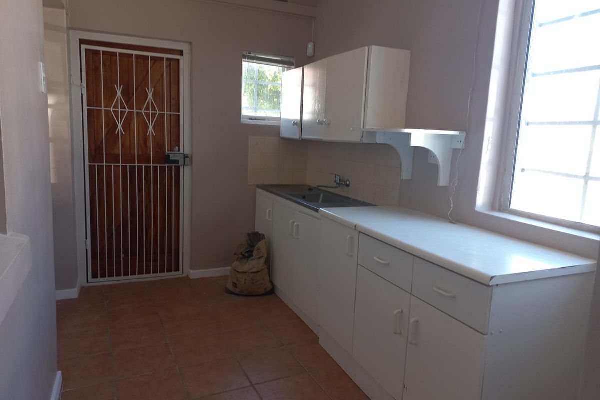 A functional kitchenette area featuring built-in cabinetry, a stainless steel sink, and tiled flooring, providing a practical utility space for office staff.