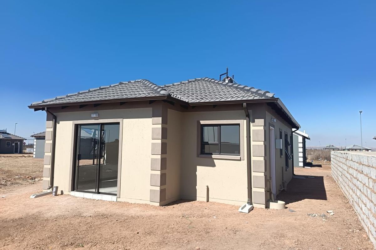 Rear view of a modern single-story house featuring a tiled roof, sliding glass doors, and aluminium window frames, set on an unlandscaped plot.