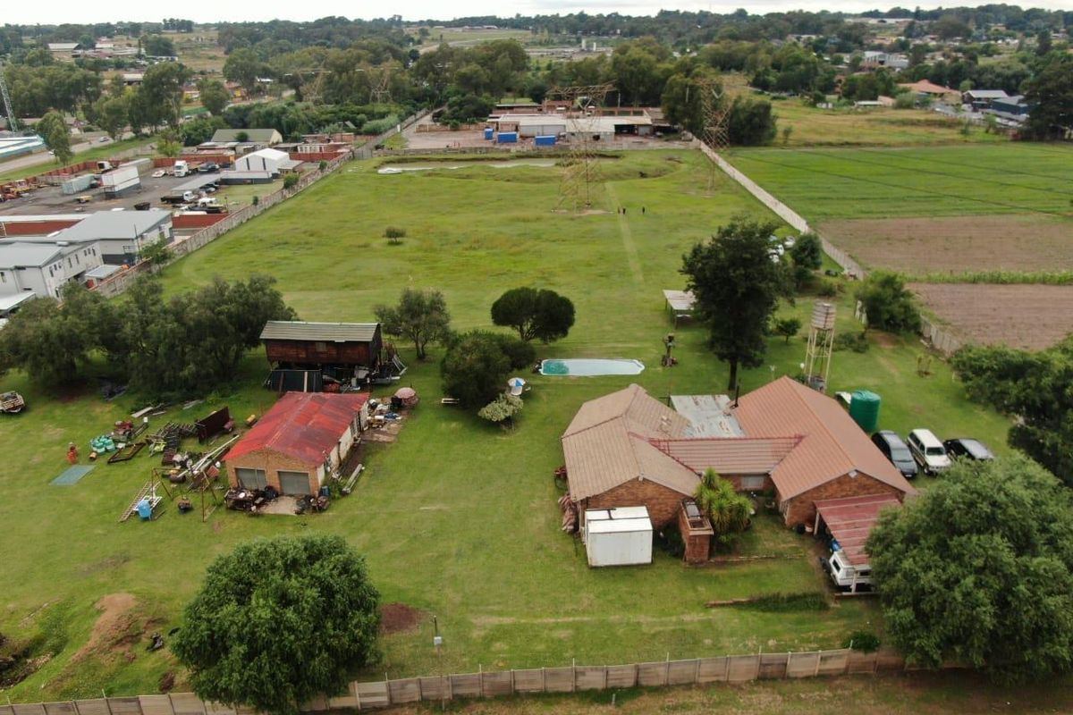 Aerial view of a small holding property featuring a main residence, outbuildings, swimming pool, and expansive grounds with perimeter fencing.