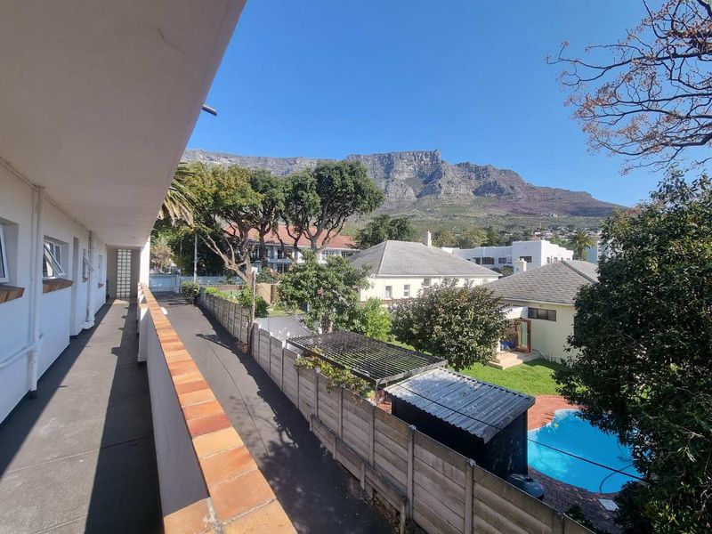 An elevated balcony walkway overlooking the surrounding residential area, garden, and swimming pool with a clear view of Table Mountain.