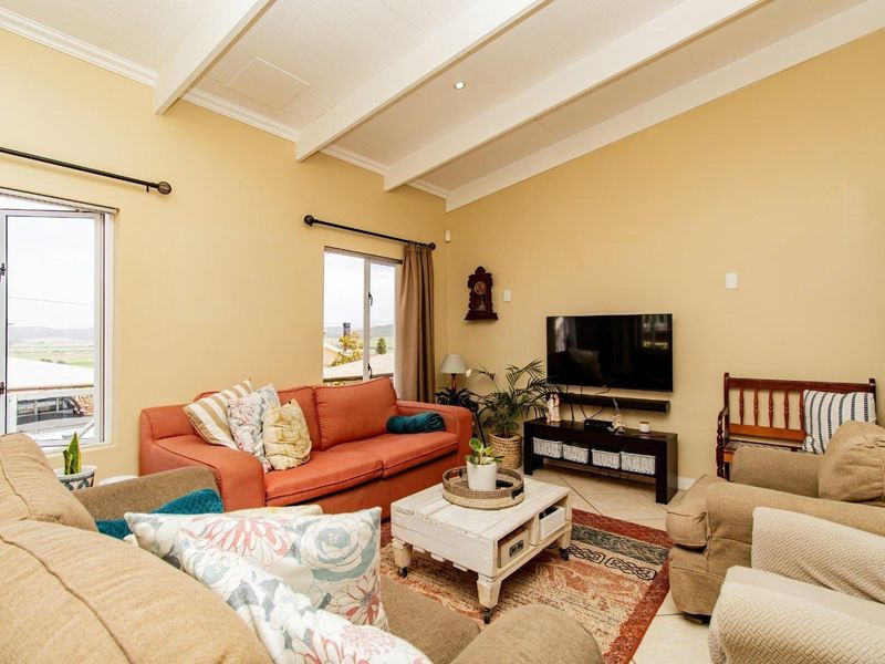 A comfortable living room featuring exposed ceiling beams, tiled flooring, and natural light through aluminium-framed windows.