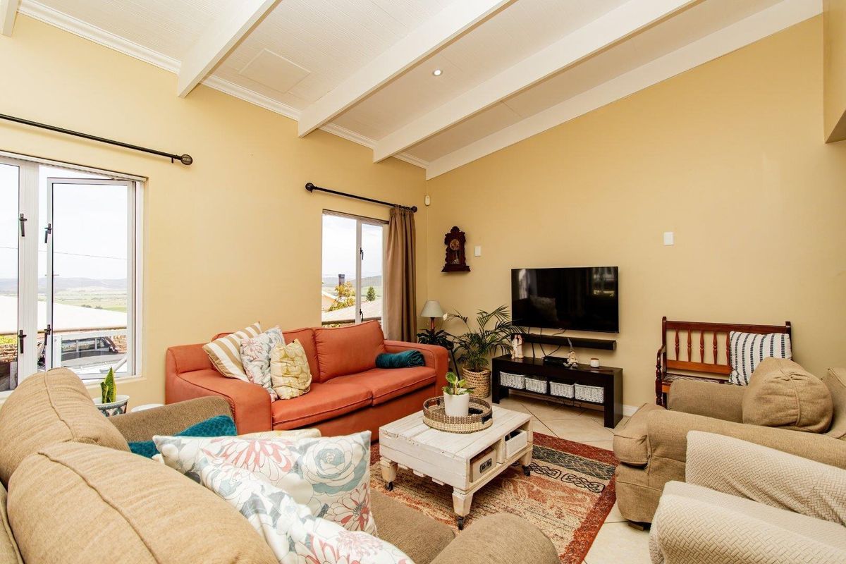A comfortable living room featuring exposed ceiling beams, tiled flooring, and natural light through aluminium-framed windows.