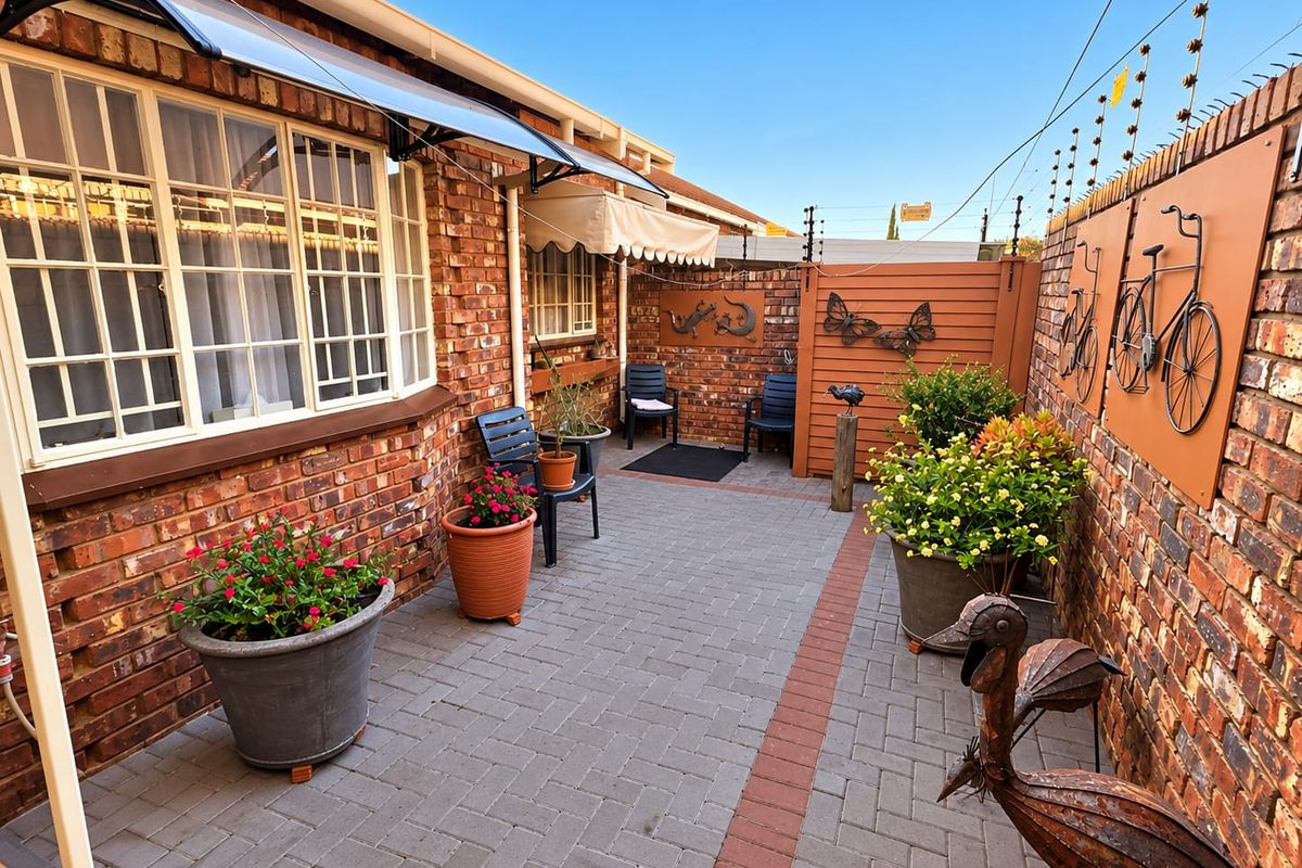 A well-maintained paved rear courtyard featuring facebrick walls, secure electric fencing, and a protective awning over the window area.