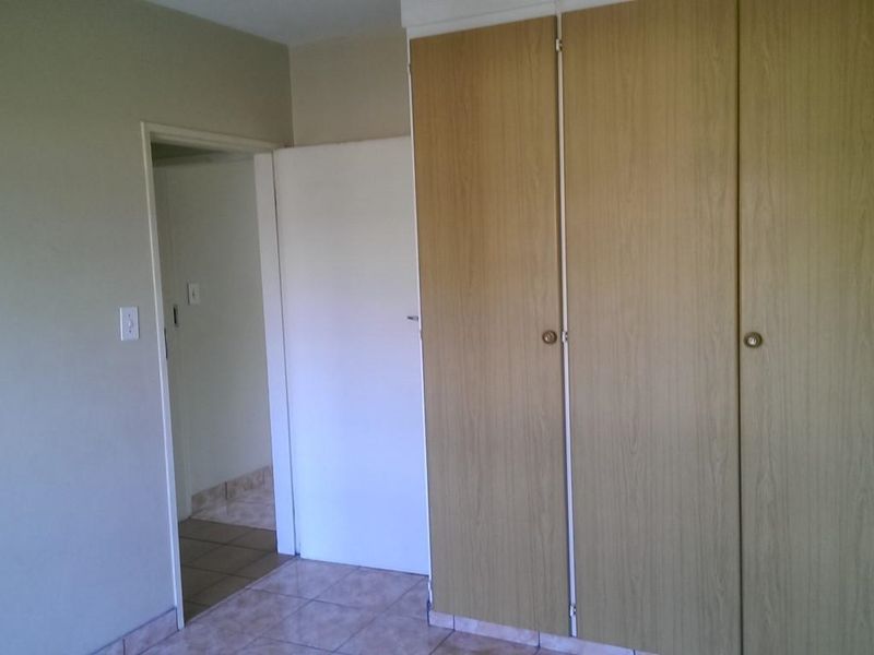 A simple bedroom interior featuring built-in wooden cupboards and tiled flooring, presenting a clean and functional space ready for personalization.