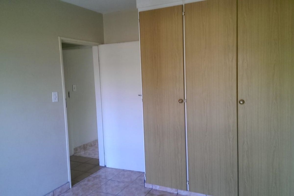 A simple bedroom interior featuring built-in wooden cupboards and tiled flooring, presenting a clean and functional space ready for personalization.