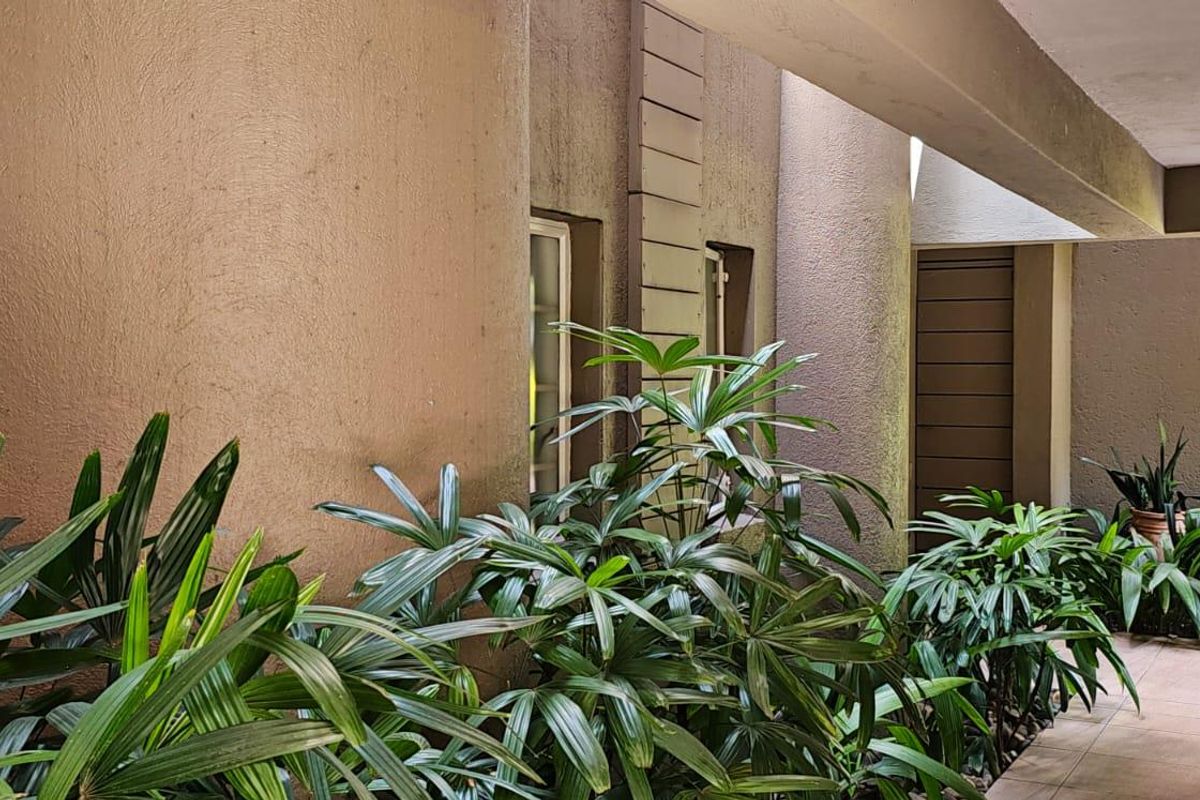A covered outdoor walkway or corridor featuring tiled flooring and textured walls, providing access to the apartment entrance.