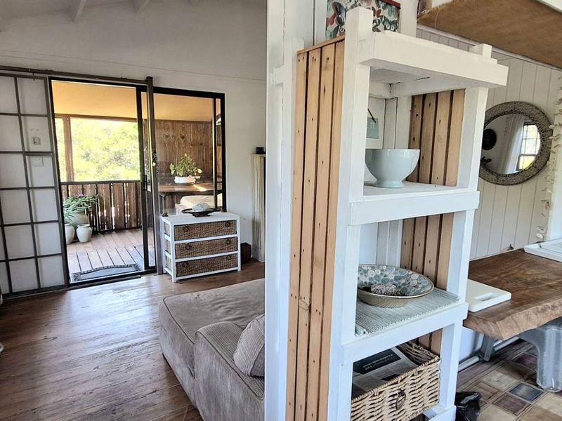 Open plan living area featuring timber flooring, exposed beam ceilings, and sliding glass doors leading to an outdoor deck.