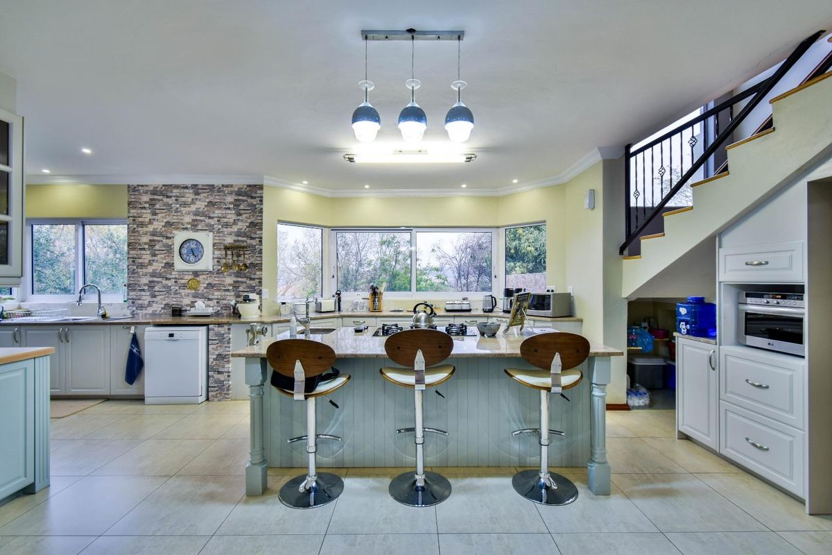Spacious kitchen featuring a central island with breakfast bar, stone countertops, built-in oven, and integrated cabinetry, set under a staircase with natural light.