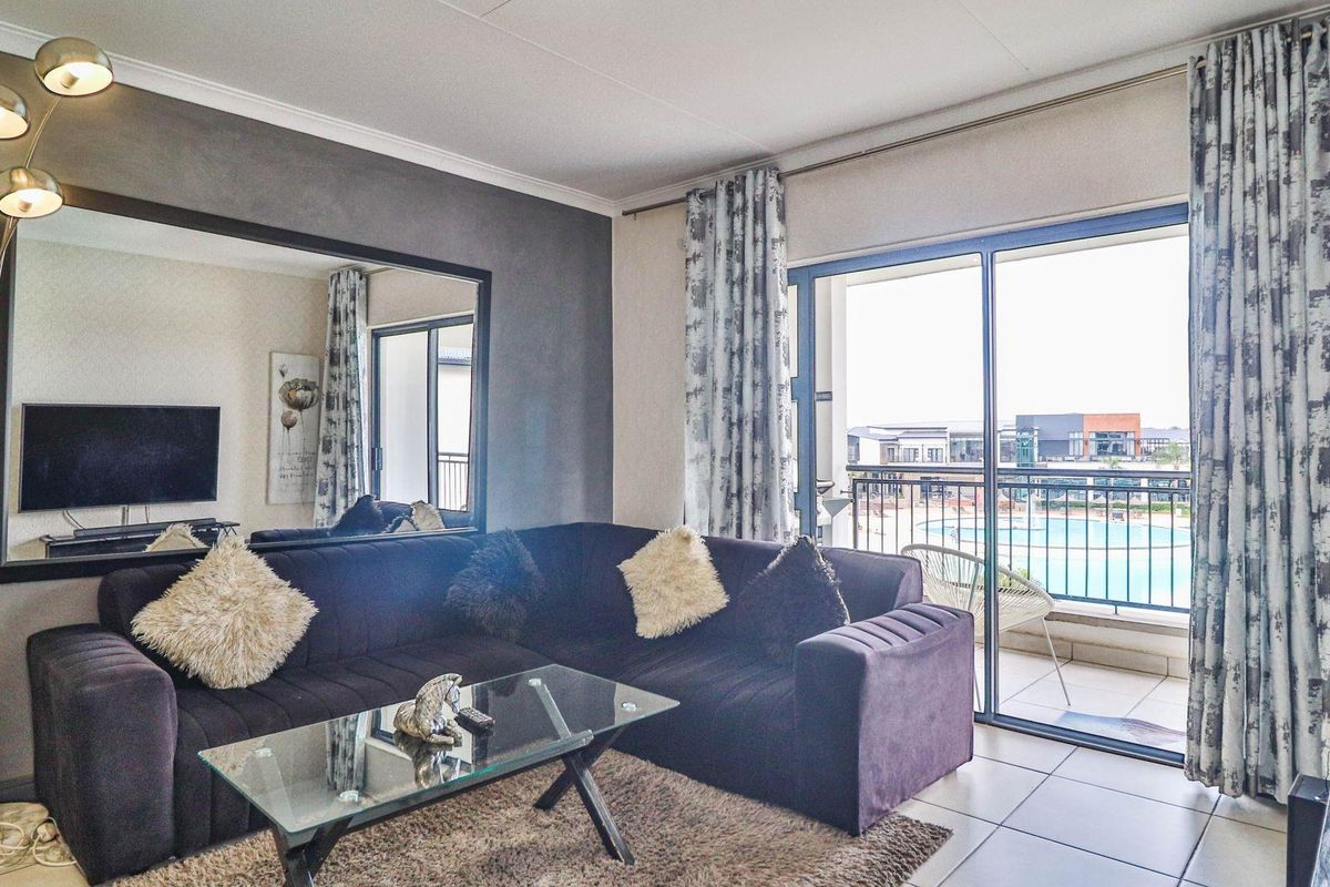 A well-lit living room featuring large sliding glass doors that open onto a balcony with views of the complex pool area.