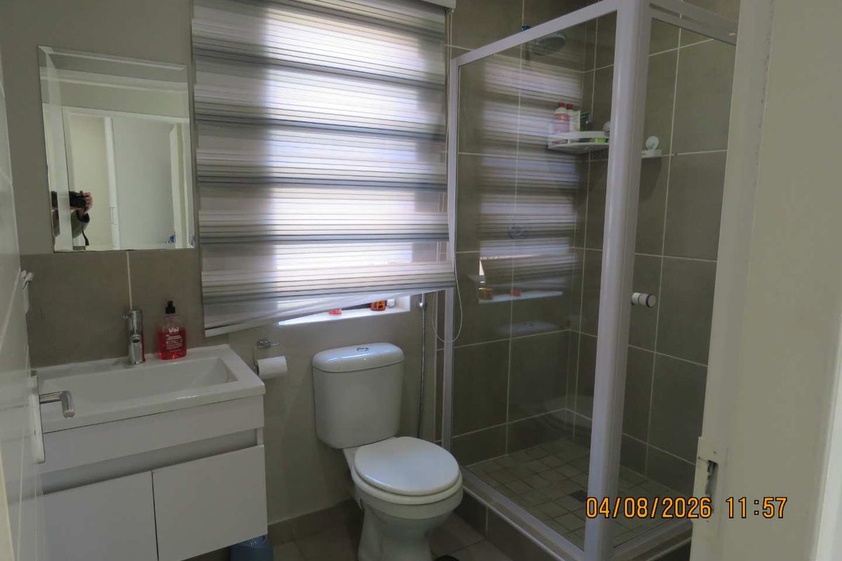 A functional bathroom featuring a modern vanity cabinet, a glass-enclosed shower, and neutral wall tiling with a roller blind for privacy.