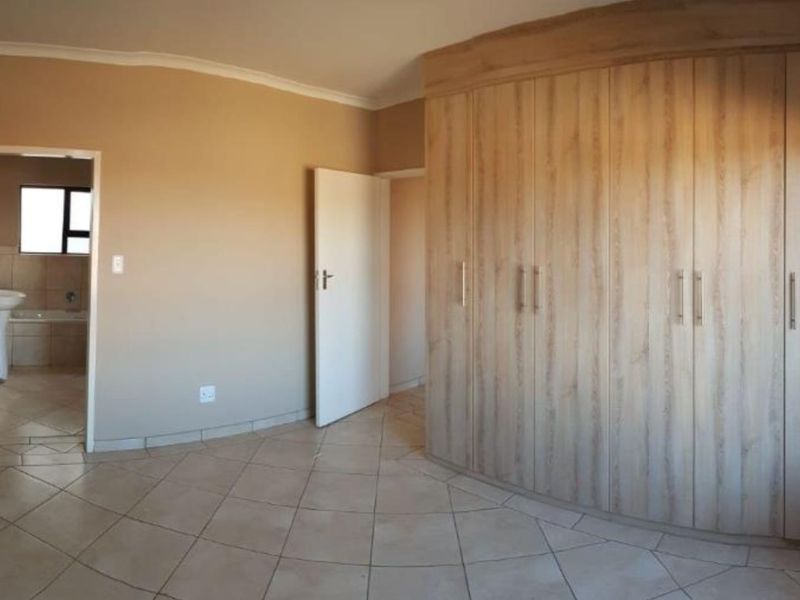 A spacious bedroom featuring built-in wooden cupboards, tiled flooring, and an adjoining en-suite bathroom.