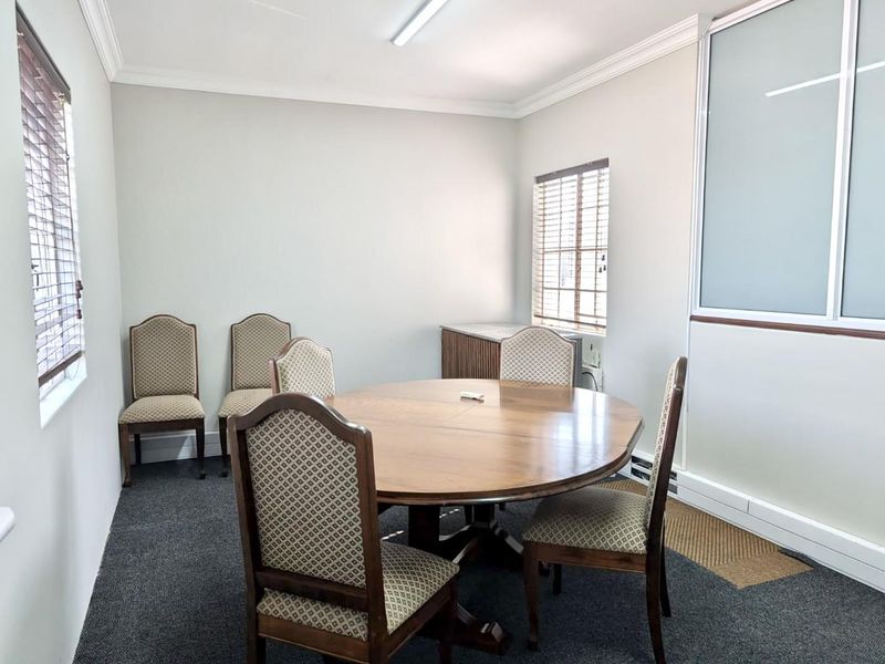 A functional office space featuring carpeted flooring, venetian blinds, and a partition wall, suitable for a meeting room or private workspace.