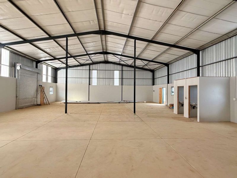 Spacious industrial warehouse featuring a high-clearance steel portal frame, concrete flooring, roller shutter access, and integrated internal washroom facilities.