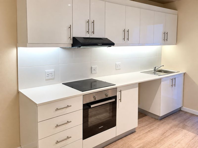 Modern kitchen featuring white high-gloss cabinetry, integrated Bosch oven and hob, extractor fan, and a stainless steel sink with under-cabinet lighting.
