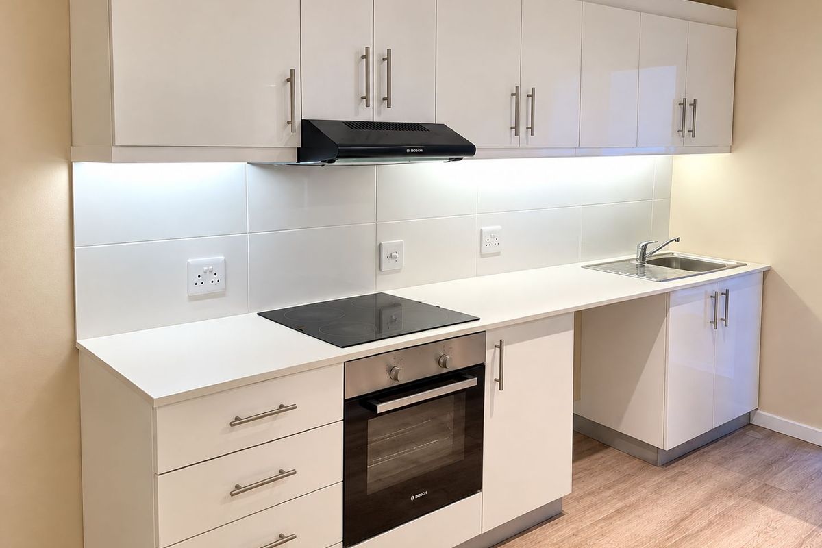 Modern kitchen featuring white high-gloss cabinetry, integrated Bosch oven and hob, extractor fan, and a stainless steel sink with under-cabinet lighting.