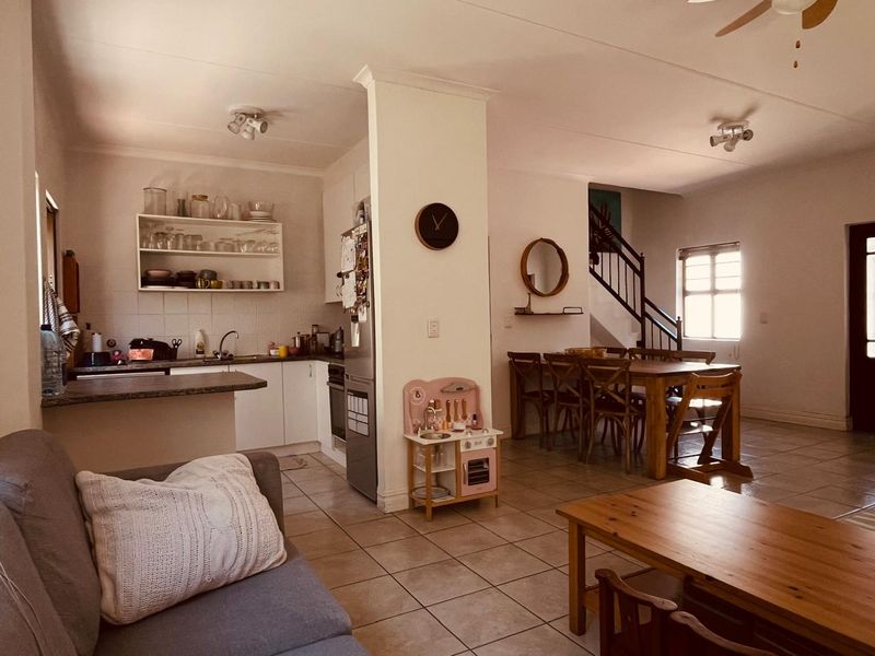 Open-plan living area featuring a functional kitchen with built-in cabinetry, tiled flooring throughout, and a staircase leading to the upper level.