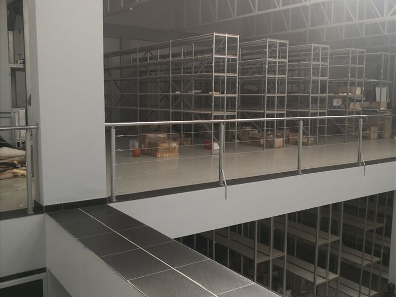 Industrial warehouse space featuring a mezzanine level with extensive metal shelving, stainless steel railings, and exposed roof trusses.