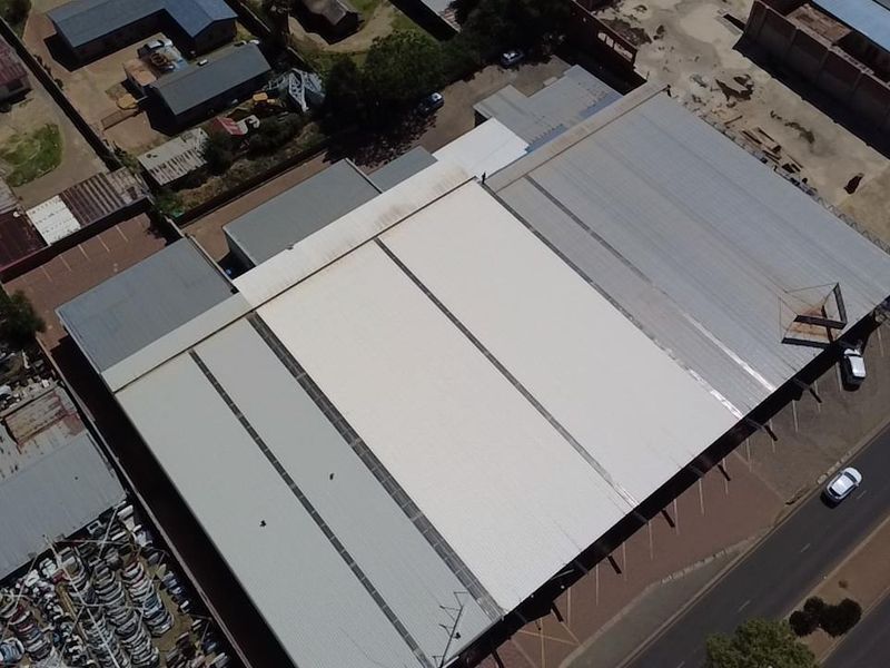 Aerial view of a commercial retail property featuring a large corrugated metal roof and adjacent paved parking area.