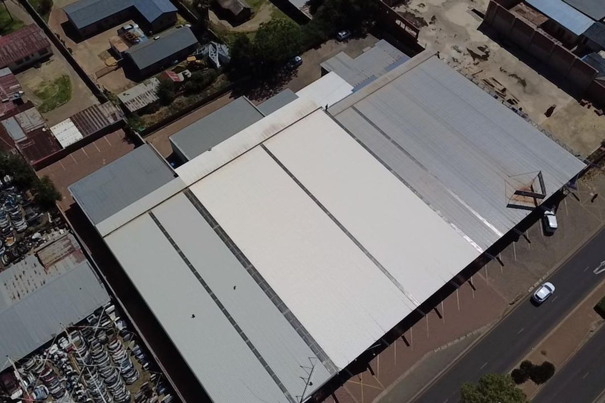 Aerial view of a commercial retail property featuring a large corrugated metal roof and adjacent paved parking area.