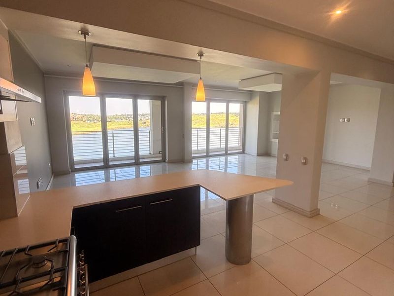 Spacious open-plan kitchen and living area featuring modern cabinetry, a gas hob, tiled floors, and large sliding doors leading to a balcony with views.