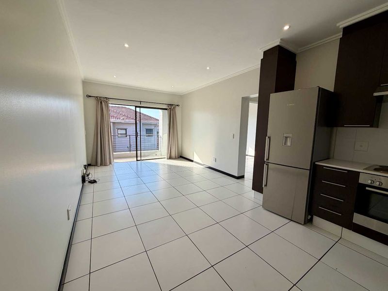 Open-plan living area featuring tiled floors, recessed lighting, and a modern kitchen with built-in cabinetry, leading to a balcony through sliding glass doors.