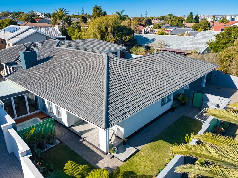 Aerial view of a residential property featuring a tiled roof, covered patio area, paved driveway, and landscaped garden.
