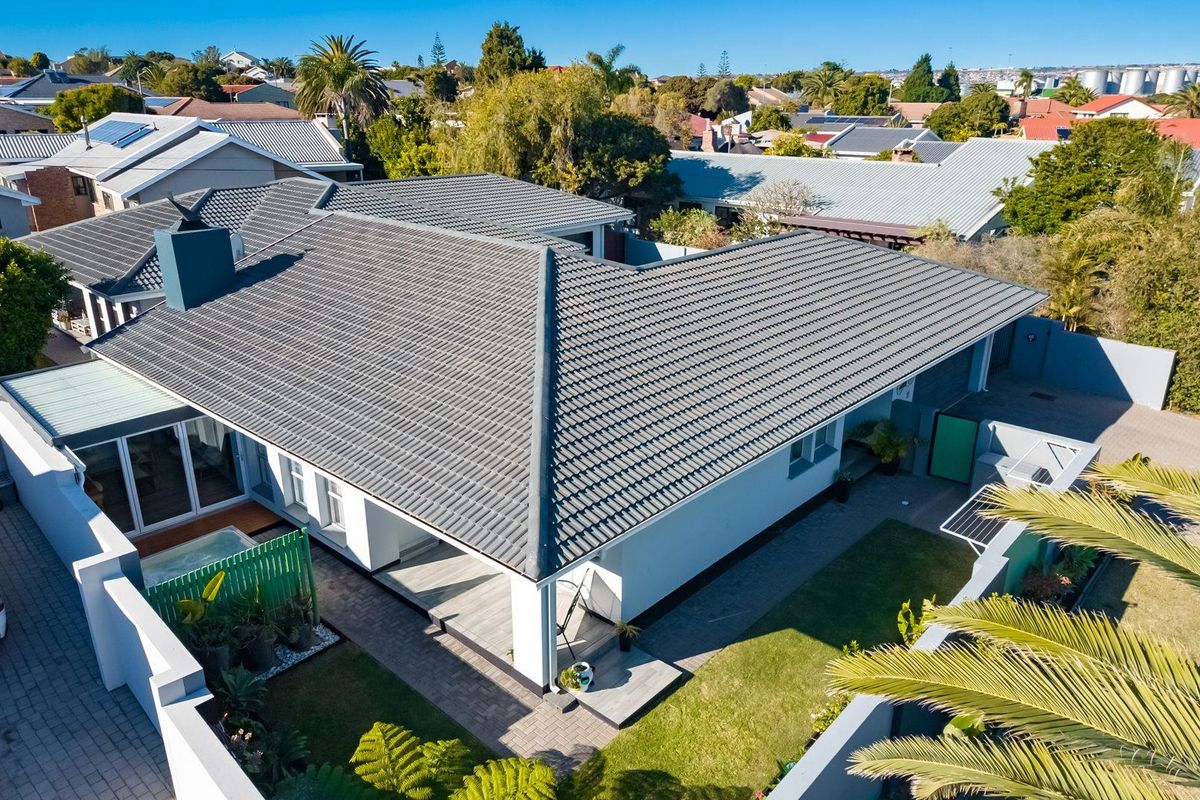 Aerial view of a residential property featuring a tiled roof, covered patio area, paved driveway, and landscaped garden.