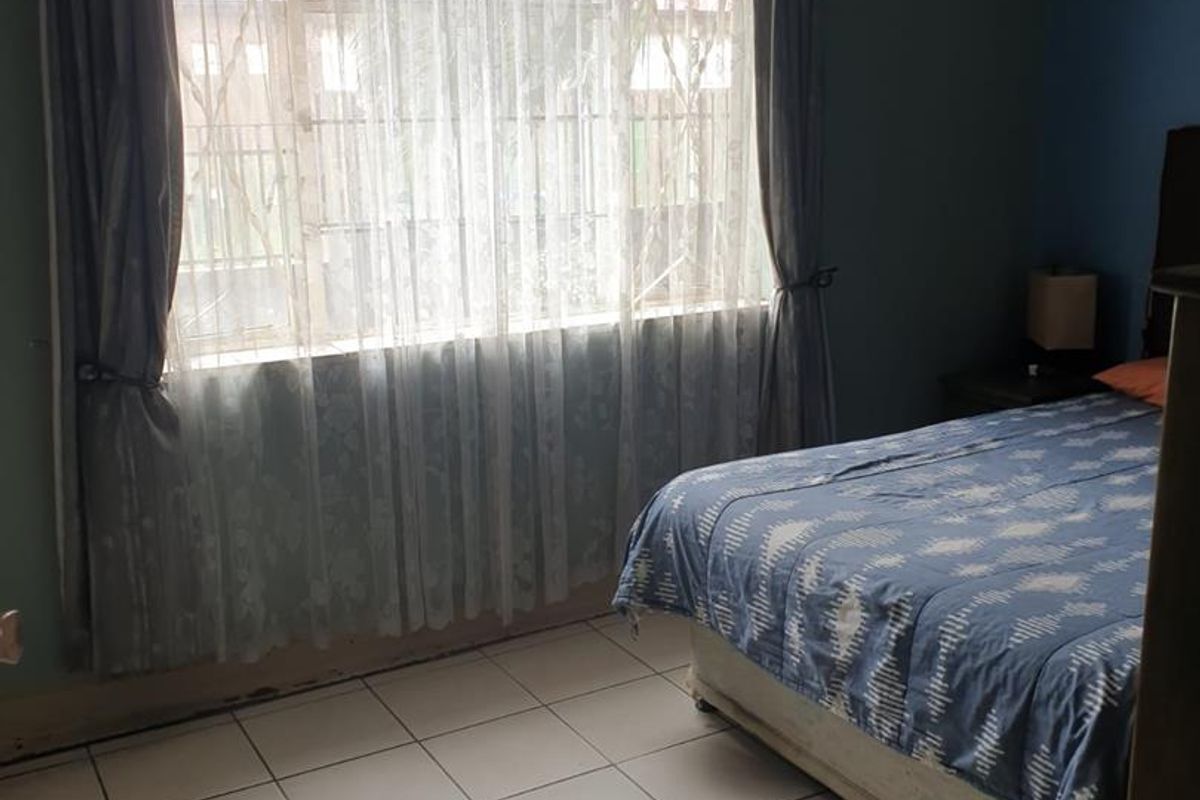 A bedroom featuring tiled flooring, a large window with security bars, and blue painted walls.