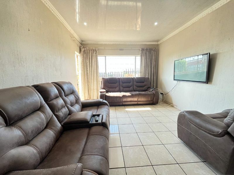 A living room featuring tiled flooring, recessed downlighting, decorative ceiling cornices, and a wall-mounted television.