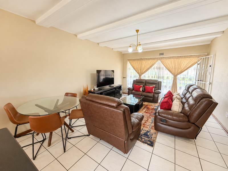 Open-plan living and dining area featuring tiled flooring, exposed beam ceilings, and direct access to a balcony through a sliding glass door.