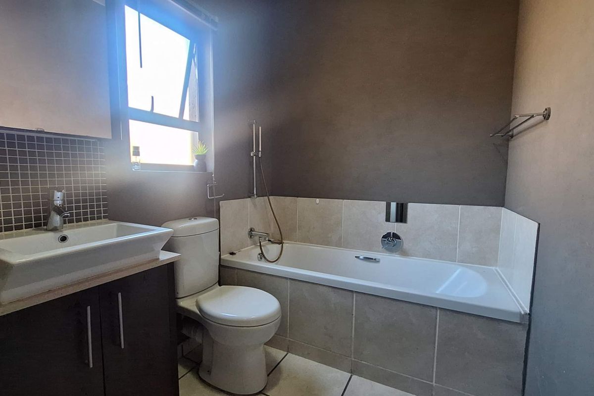 A functional bathroom featuring a vanity with basin, a standard toilet, and a tiled bathtub with shower mixer.